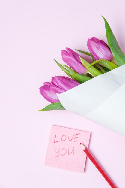 Tulipani viola e biglietto di auguri su sfondo rosa Concetto di primavera Vista dall'alto spazio piatto per la copia