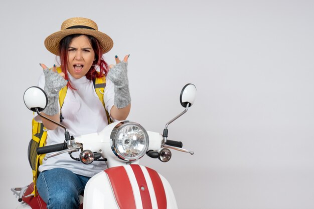 Turista femminile di vista frontale che si siede e che posa sulla motocicletta sulla parete bianca