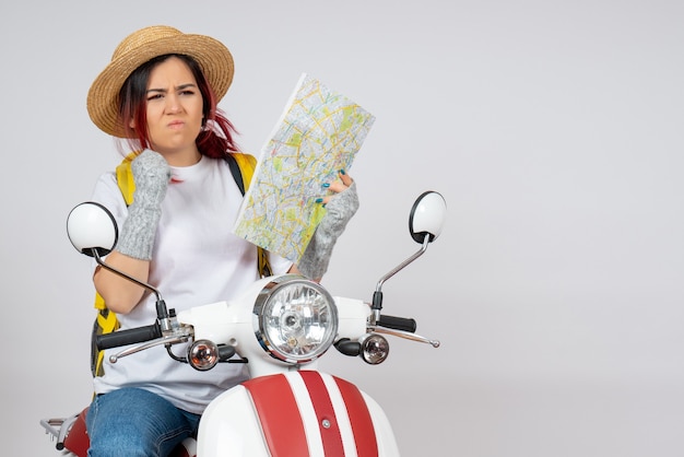 Turista femminile di vista frontale che si siede sulla motocicletta con la parete bianca della mappa