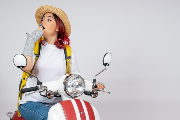 Turista femminile di vista frontale che si siede sulla motocicletta sulla parete bianca