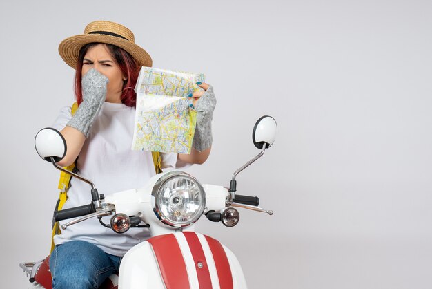 Turista femminile di vista frontale che si siede sulla parete bianca della mappa della tenuta della motocicletta