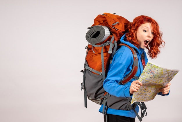 Turista femminile di vista frontale che va in viaggio in montagna con zaino e mappa