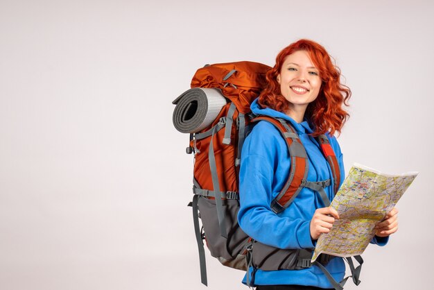 Turista femminile di vista frontale che va in viaggio in montagna con zaino e mappa