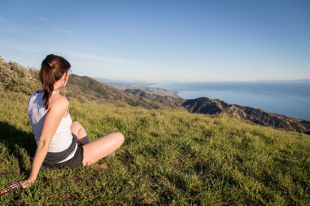 Turista femminile seduto in cima al sentiero escursionistico Gaviota Peak che si affaccia sulla costa della California