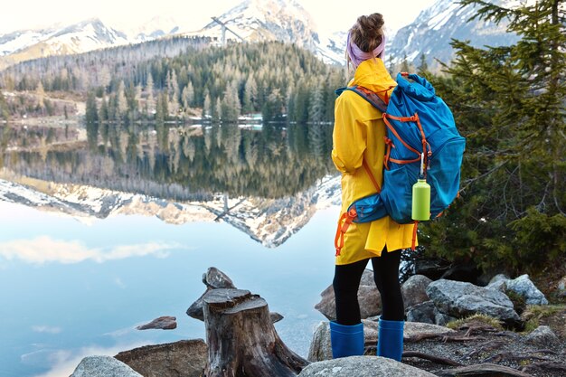Turista femminile si trova sulla riva del bellissimo lago di montagna, gode di paesaggi maestosi e natura
