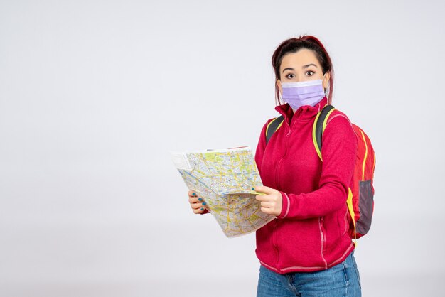 Turista femminile vista frontale con mappa in maschera sul muro bianco