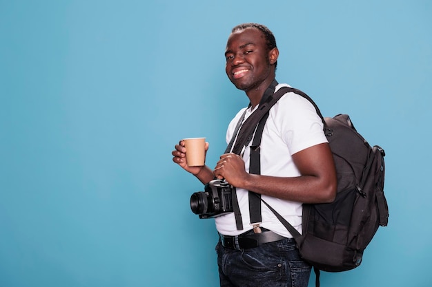 Turista gioioso che ha un dispositivo DSLR mentre è eccitato per la vacanza in città. Sorridente appassionato di fotografia che indossa uno zaino da viaggio e una fotocamera professionale pronta per il viaggio di vacanza.