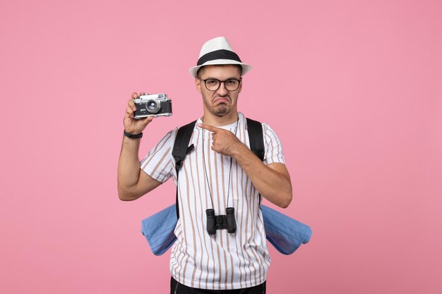 Turista maschio di vista frontale che prende immagine con la macchina fotografica sul colore rosa delle emozioni turistiche della parete