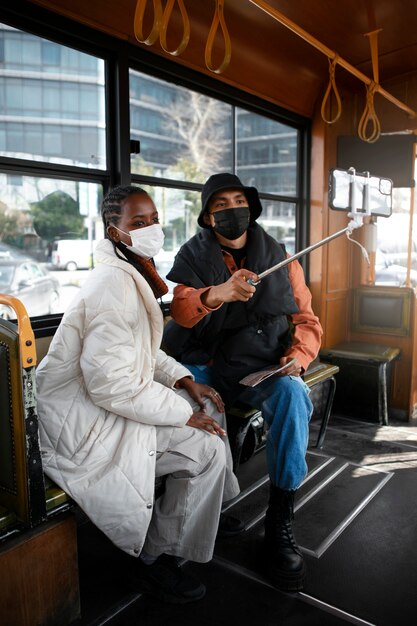 Turisti maschi e femmine che si fanno selfie sull'autobus mentre indossano maschere mediche