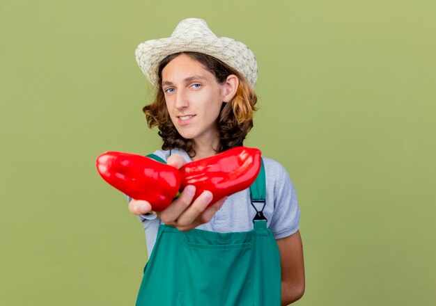 Tuta da portare dell'uomo del giovane giardiniere e cappello che mostrano i peperoni dolci rossi