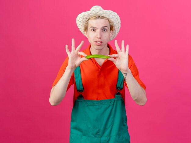 Tuta da portare dell'uomo del giovane giardiniere e cappello che mostrano sorridere verde del peperoncino