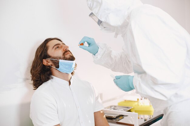 Tuta protettiva per medico e maschera chirurgica per il viso. Tampone di cotone dalla gola e dal naso del paziente. Test del coronavirus, test per l'infezione da covid-19 in una pandemia.