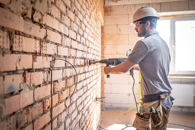 Tuttofare in un cantiere in procinto di perforare un muro con un perforatore.