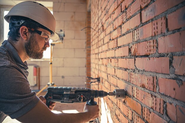 Tuttofare in un cantiere nel processo di perforazione di un muro con un perforatore.