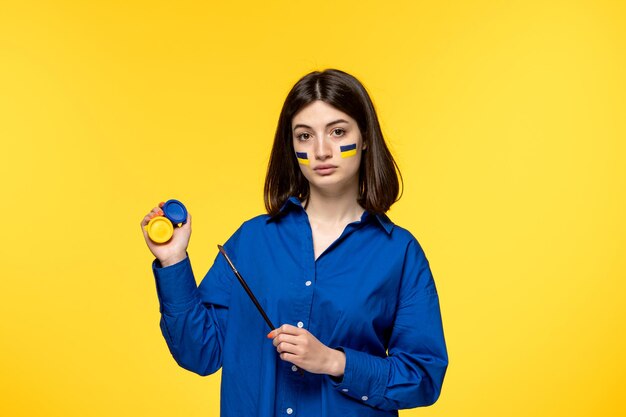 Ucraina conflitto russo capelli scuri ragazza carina con bandiere sulle guance in possesso di vernici blu e gialle