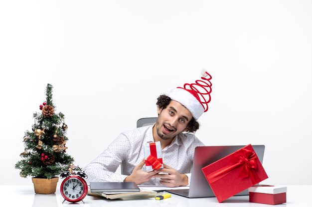 Umore di Natale con felice giovane imprenditore positivo con cappello di Babbo Natale e tenendo il suo dono di brainstorming su sfondo bianco