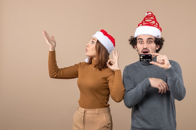 umore di natale con le coppie fredde sorprese soddisfatte eccitate che indossano cappelli rossi di Babbo Natale che mostrano carta di credito