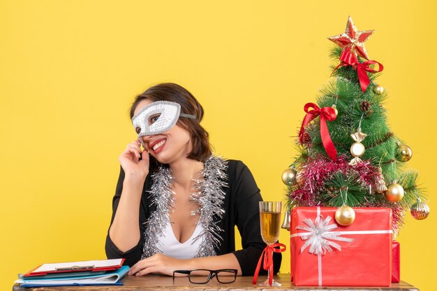 Umore di nuovo anno con sorridente affascinante signora in tuta che indossa la maschera in ufficio su giallo isolato