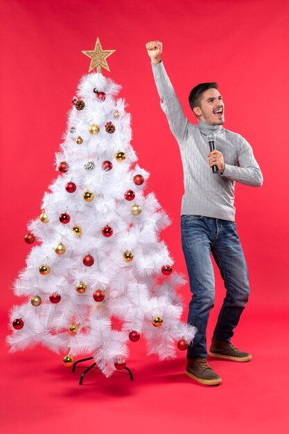 umore natalizio con ragazzo fiducioso vestito in jeans in piedi vicino all'albero di Natale decorato e orgoglioso di se stesso