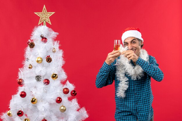 umore natalizio con un giovane pazzo con cappello di Babbo Natale e alzando un bicchiere di vino si rallegra vicino all'albero di Natale