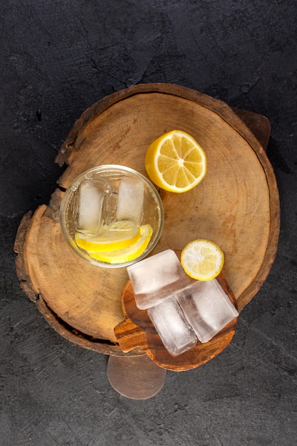 Un'acqua vista dall'alto con limone fresca bevanda fresca all'interno di vetro con cubetti di ghiaccio con fette di limoni sullo sfondo scuro cocktail bere frutta