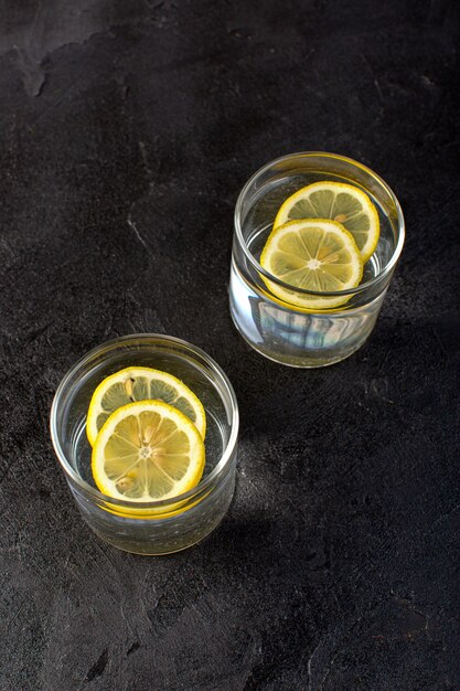 Un'acqua vista frontale con bevanda al limone con limoni a fette all'interno di bicchieri trasparenti sul buio