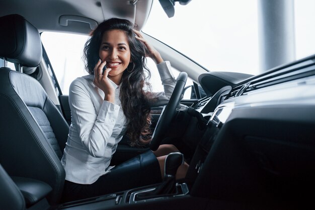 Un amico sta chiamando. Bella donna di affari che prova la sua nuova automobile nel salone dell'automobile