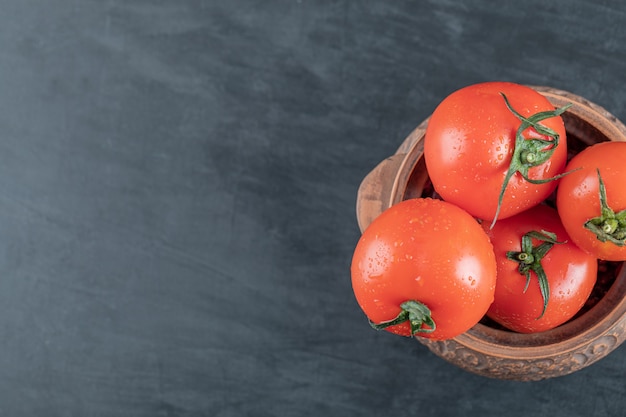 Un'antica pentola con pomodori freschi su sfondo scuro.