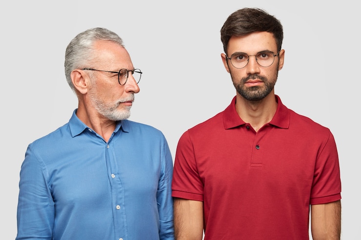 Foto gratuito un anziano maschio esperto guarda attentamente suo figlio adulto, dà consigli, indossa occhiali e camicia blu formale, ha buoni rapporti