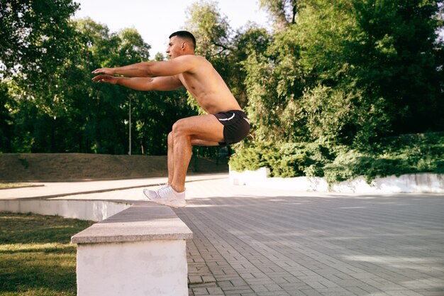 Un atleta maschio muscoloso che fa allenamento al parco. Ginnastica, allenamento, flessibilità allenamento fitness. Città estiva in una giornata di sole sul campo spaziale