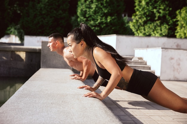 Un atleta muscoloso che fa allenamento al parco. Ginnastica, allenamento, flessibilità allenamento fitness. Città estiva in una giornata di sole sul campo di sfondo. Stile di vita attivo e sano, gioventù, bodybuilding.