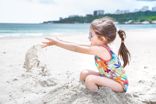 Un bambino piccolo che lancia la sabbia in riva al mare. Divertimento estivo e ricreazione.