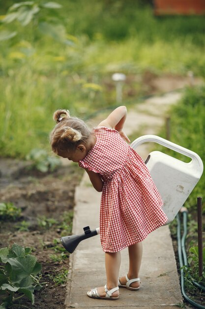 Un bambino piccolo con un annaffiatoio con fiori versare. Ragazza con un imbuto. Bambino in un vestito rosa.