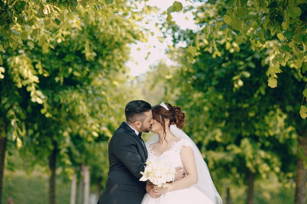 Un bel giovane che indossa un abito nero e una barba nel parco insieme alla sua sposa