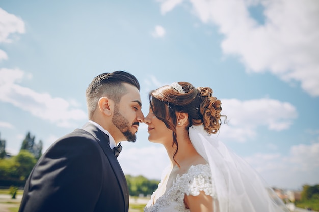 Un bel giovane che indossa un abito nero e una barba nel parco insieme alla sua sposa