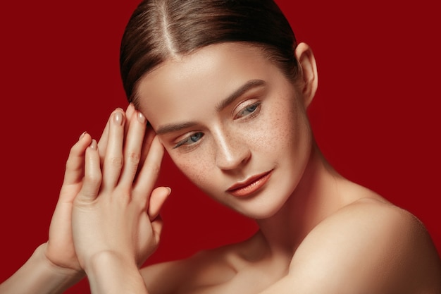 Un bel volto femminile. Pelle perfetta e pulita di giovane donna caucasica su sfondo rosso studio.