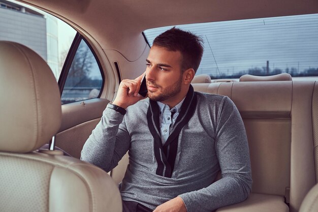 Un bell'uomo d'affari in abiti eleganti che lavora, parlando al telefono mentre è seduto in macchina.