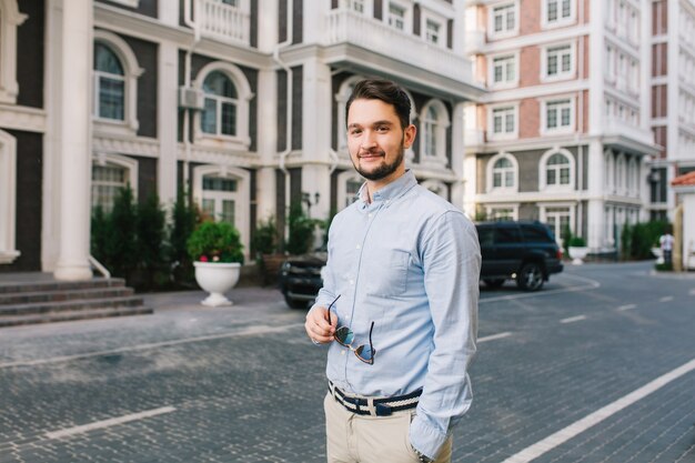 Un bell'uomo dai capelli scuri in camicia blu sta camminando per il quartiere britannico. Tiene gli occhiali da sole