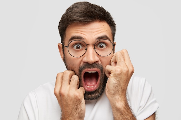 Un bell'uomo emotivo con la barba lunga urla ad alta voce, apre ampiamente la bocca, esclama stupefatto