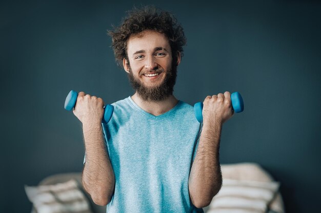 Un bell'uomo fa fitness con i manubri a casa, il ragazzo si tiene in forma durante la quarantena