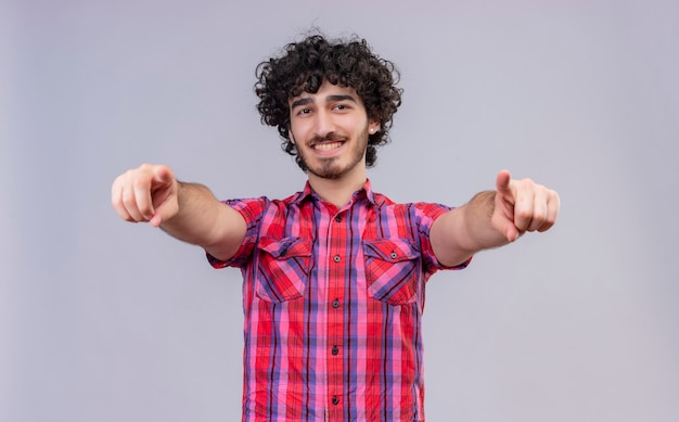 Un bell'uomo felice con i capelli ricci in camicia a quadri che punta con il dito indice verso la telecamera