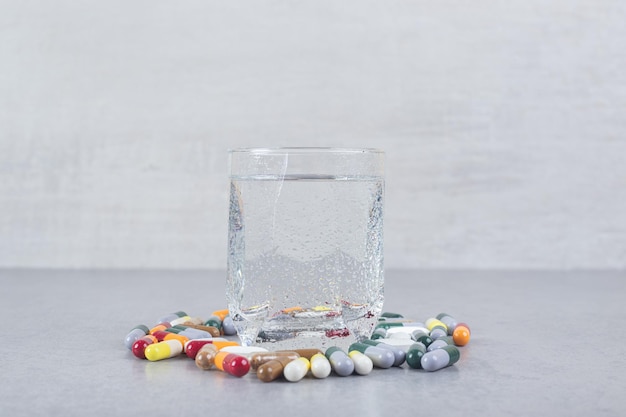 Un bicchiere di acqua pura con pillole colorate su sfondo grigio.