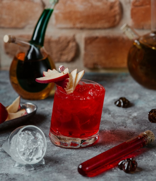 Un bicchiere di alcool rosso cocktail con fettine di mela e cubetti di ghiaccio.