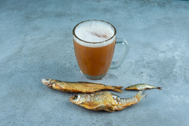 Un bicchiere di birra accanto ai pesci, sul tavolo blu.