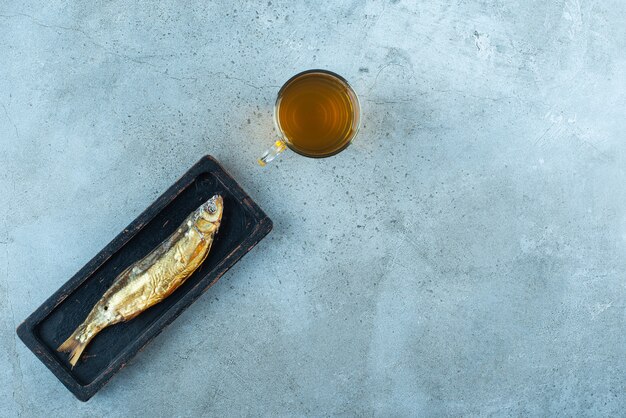 Un bicchiere di birra accanto al pesce su un piatto di legno, sul tavolo blu.