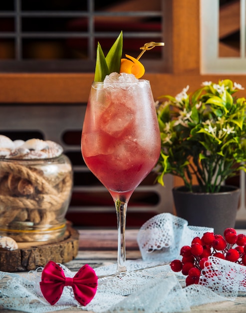 Un bicchiere di cocktail rosso con cubetti di ghiaccio e foglie verdi.