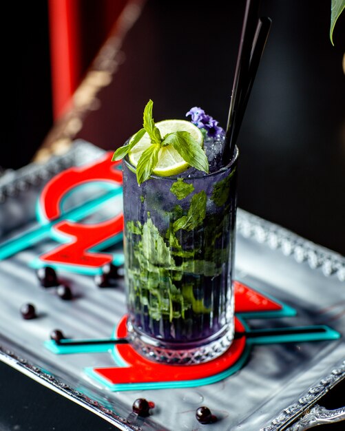 Un bicchiere di mojito viola con fiori viola lime e menta