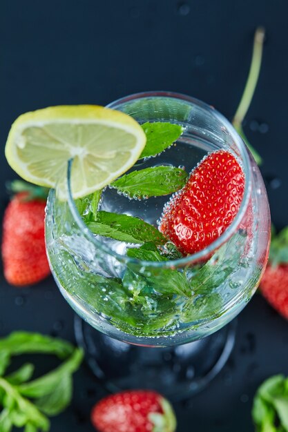 Un bicchiere di succo con frutta intera e fetta di limone all'interno su una superficie scura