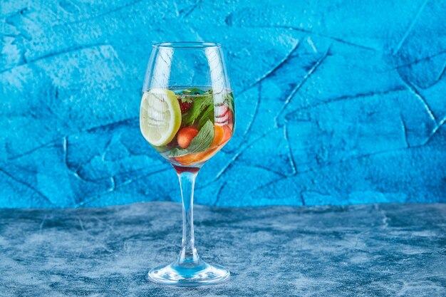 Un bicchiere di succo con frutti interi all'interno sulla superficie blu