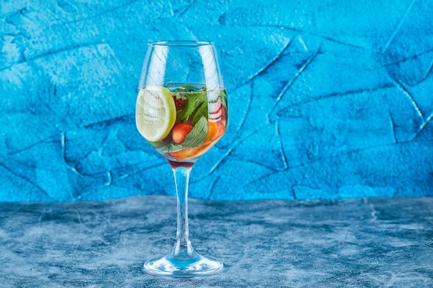 Un bicchiere di succo con frutti interi all'interno sulla superficie blu